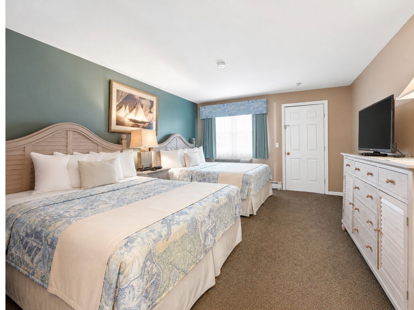 A hotel room with two beds, a television, a dresser, and a painting on the wall.