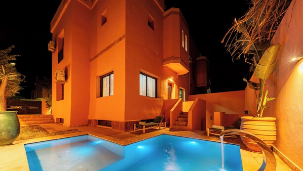 A swimming pool with a water feature, a lounge chair, and a staircase leading to a building with multiple windows. - 4 Bedroom Villa in Bab Ighli Marrakech Heated Pool Atlas View (Marrakesh)