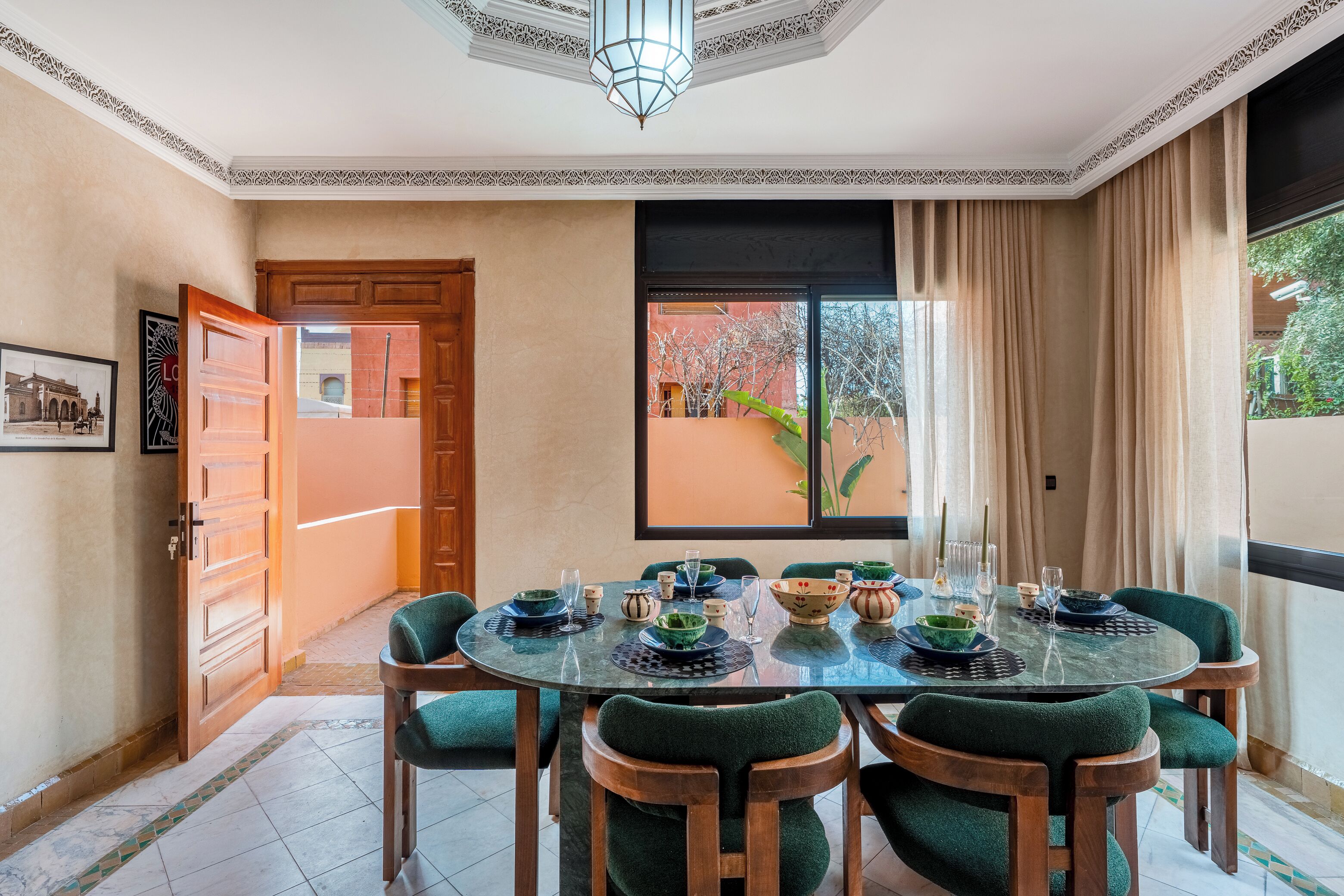 A dining area with a round table set for six, surrounded by six chairs with green upholstery.