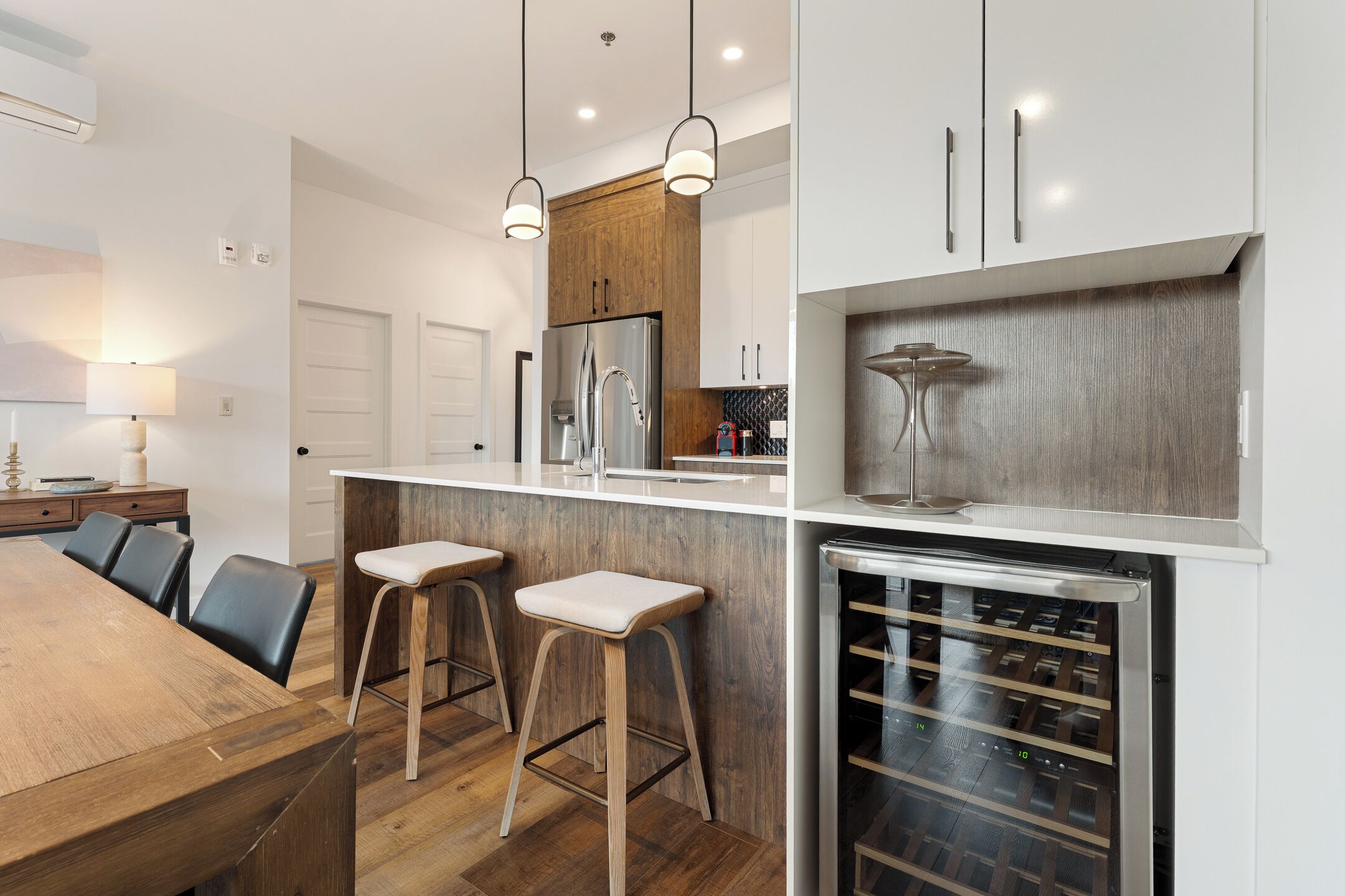 Une cuisine moderne dotée d’un îlot central en bois, de tabourets de bar, d’un réfrigérateur à vin et de luminaires suspendus.