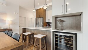 Una cocina moderna con una isla de madera, taburetes de bar, un enfriador de vino e iluminación colgante.