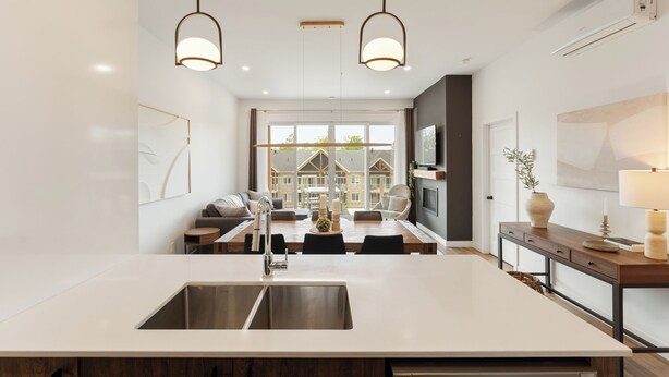 Una cocina moderna con una isla grande, luces colgantes y vistas a una casa a través de amplios ventanales.