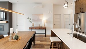 Una cocina moderna con una mesa de comedor de madera, electrodomésticos integrados y una lámpara colgante.