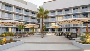 Un hôtel à plusieurs étages doté d’espaces extérieurs aménagés avec des palmiers et des parasols.
