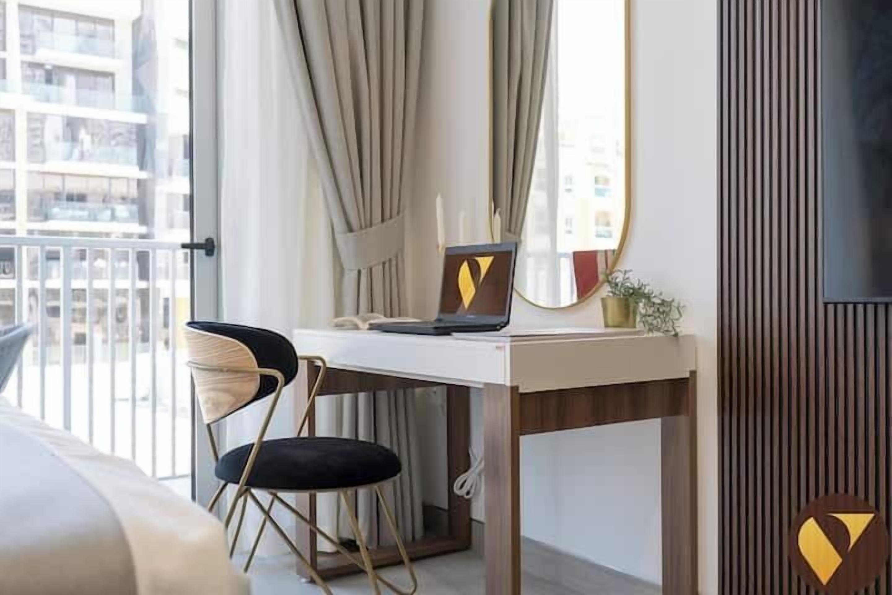 A modern hotel room with a desk, laptop, and a chair.