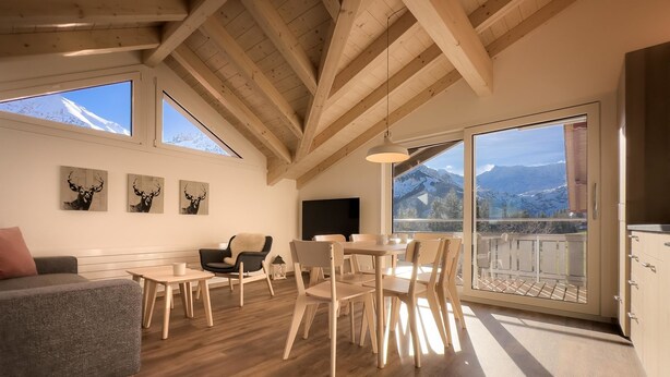 Un vaste espace de vie doté d’un haut plafond, de poutres apparentes, d’un canapé, d’une table à manger, de chaises et d’œuvres d’art accrochées aux murs.