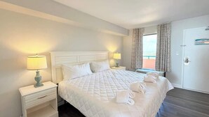 Ein Hotelzimmer mit einem großen Bett, zwei Nachttischen mit Lampen, einer Tür mit Blick und einem Fenster mit Vorhängen.
