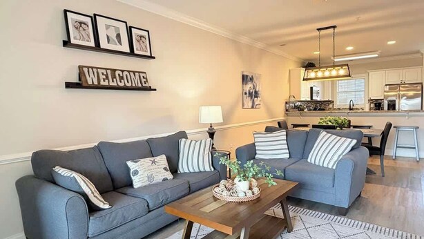 Un salon moderne avec un canapé gris, une table basse agrémentée d’une plante et un panneau « BIENVENUE » accroché au mur.