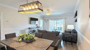 Un salon moderne avec un canapé, une table à manger avec des sets de table, un ventilateur de plafond et un téléviseur fixé au mur.