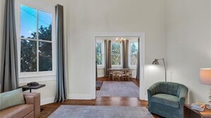 A living room with a wooden floor, a sofa, a chair, a dining table with chairs, and a chandelier. - Walk everywhere. Stay in comfort. Experience New Orleans like a local, (New Orleans)