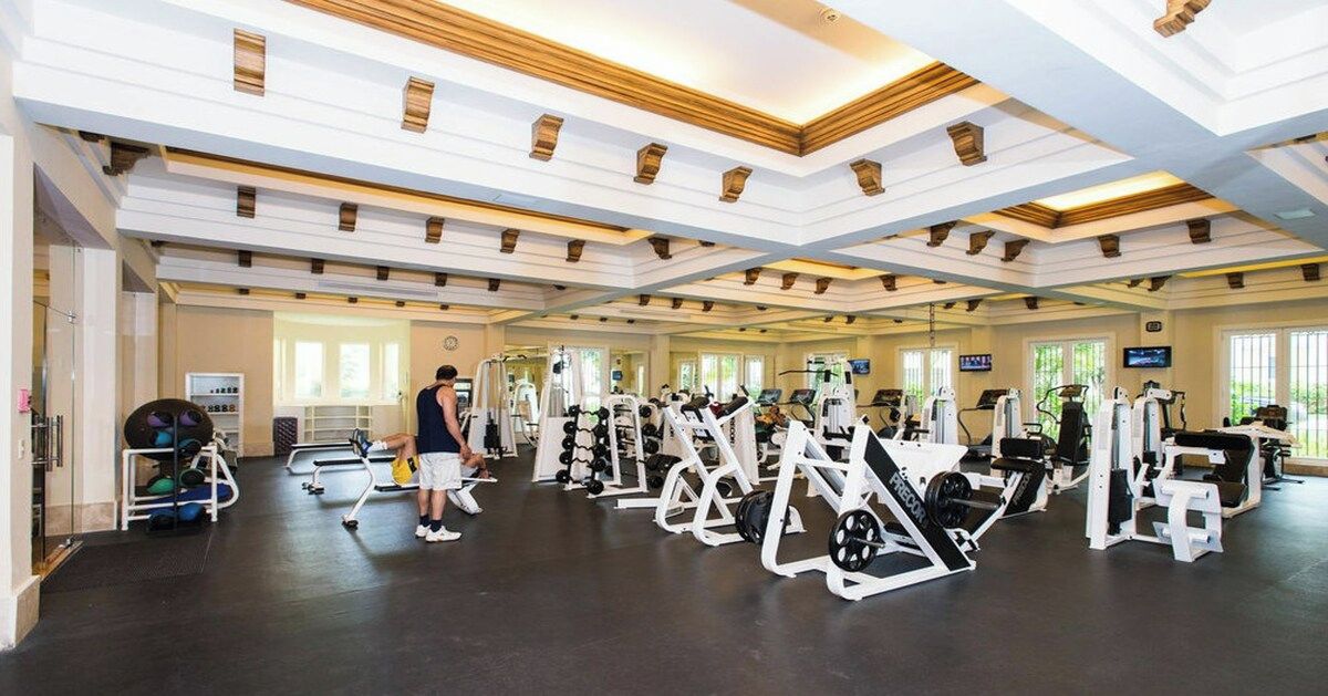 A gym with various exercise machines, a person using a machine, and a window providing natural light.