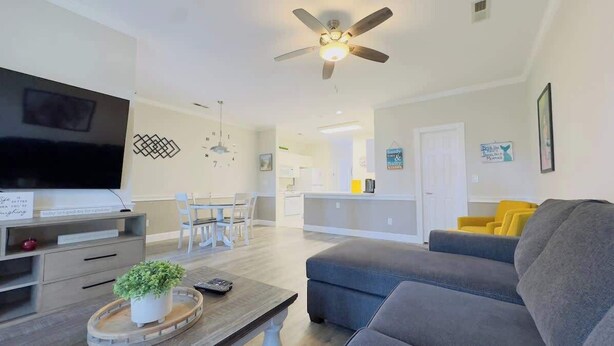 A modern living room with a flat-screen TV, a ceiling fan, and a dining area with chairs and a table. - Bright 1BR Escape, Near Beach, Golf (Myrtle Beach)