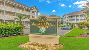 A sign for Magnolia Place with a green and gold design, surrounded by well-maintained lawns and a parking area. - Bright 1BR Escape, Near Beach, Golf (Myrtle Beach)