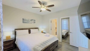 A bedroom with a bed, bedside lamps, a ceiling fan, a door, and a mirror. - Bright 1BR Escape, Near Beach, Golf (Myrtle Beach)