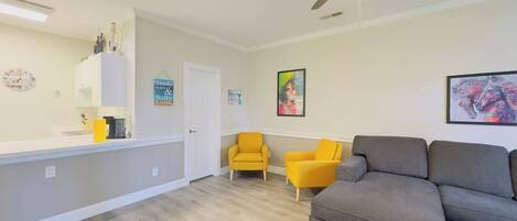 A living room with a gray sofa, two yellow armchairs, a ceiling fan, and a white cabinet with kitchen items.