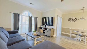 A modern living room with a sofa, coffee table, TV, and dining area. - Bright 1BR Escape, Near Beach, Golf (Myrtle Beach)