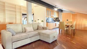 A modern living room with a sectional sofa, a dining area with a table and chairs, and a kitchen in the background. - Loft Piazza Maggiore, comfort in the city center (Bologna)
