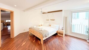 A spacious bedroom with a wooden bed, a ceiling fan, and a large window with a view of the outside. - Loft Piazza Maggiore, comfort in the city center (Bologna)