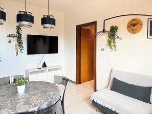 Moderni olohuone, jossa on pyöreä ruokapöytä, sohva ja seinälle asennettu televisio.