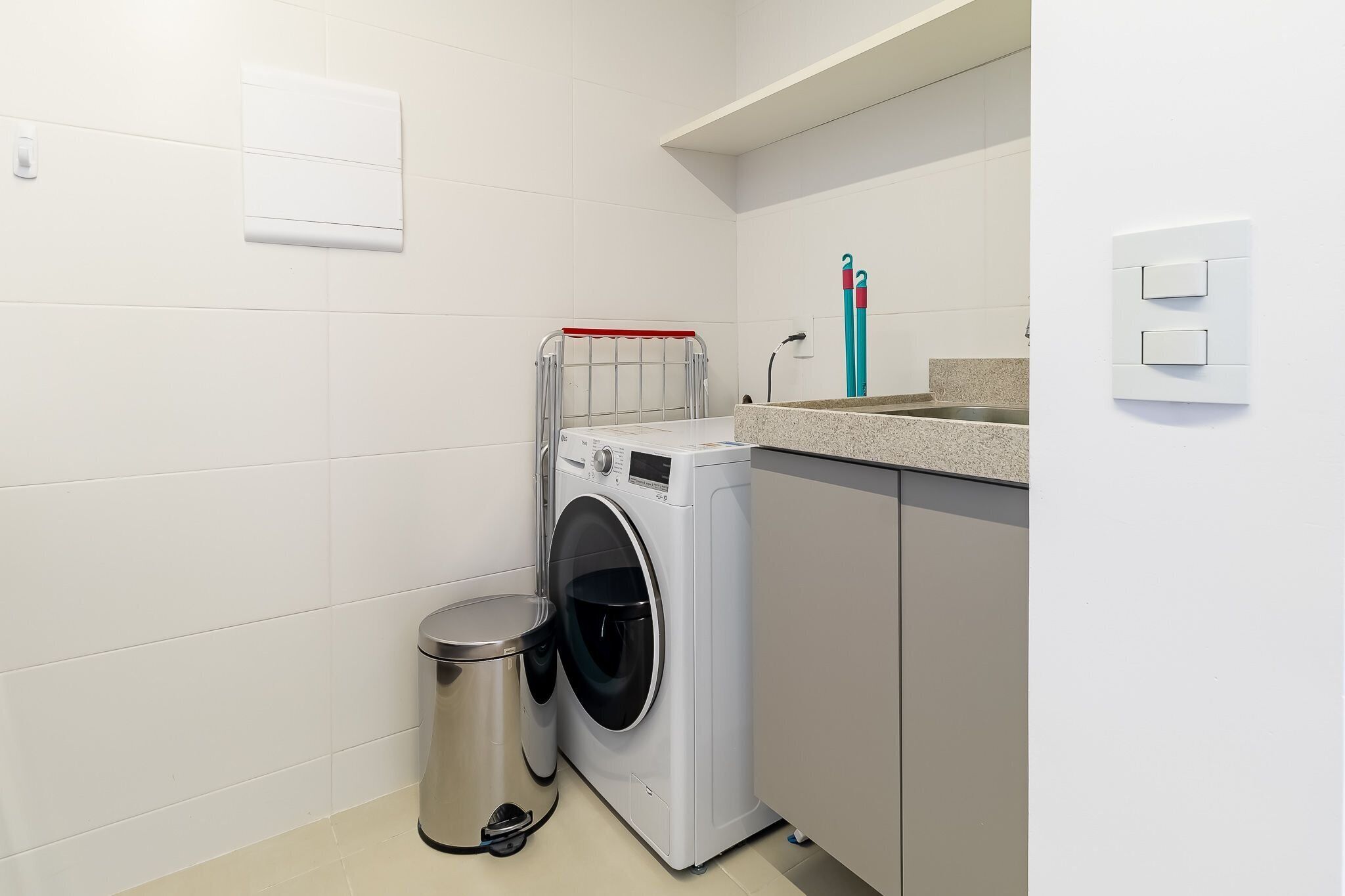 Uma lavanderia compacta com máquina de lavar, lixeira e bancada.