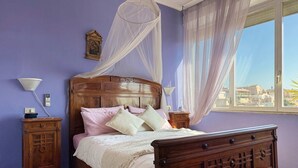 A bedroom with a wooden bed, a nightstand, a bedside table, a window with sheer curtains, and a city view. - Belsito Terrace, Rome Skyline (Roma)