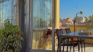 A balcony with a table and chairs, a potted plant, and a view of buildings in the distance. - Belsito Terrace, Rome Skyline (Roma)