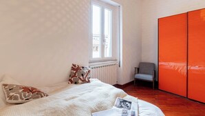 Ein Schlafzimmer mit Bett, Fenster, Heizkörper, Stuhl und Kleiderschrank.