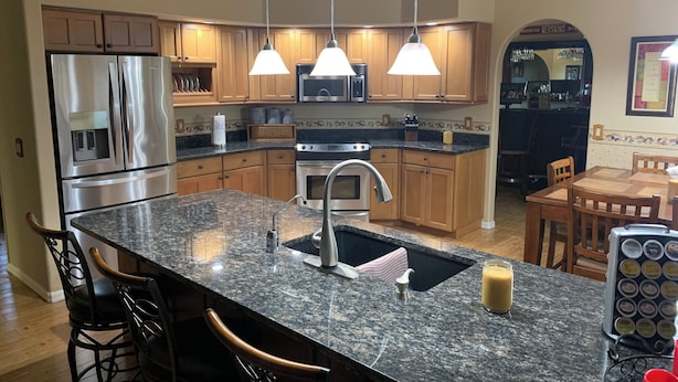 Una cocina moderna con encimeras de granito, electrodomésticos de acero inoxidable, armarios de madera e iluminación colgante.