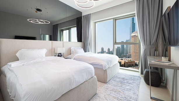 A modern hotel room with two beds, a large window with a city view, a contemporary light fixture, and a small table with a vase. - Luxury 2BR Burj Khalifa View Dubai Mall (Dubai)