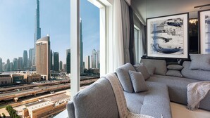 A modern living room with a large window, a grey sofa, and a framed abstract painting. - Luxury 2BR Burj Khalifa View Dubai Mall (Dubai)