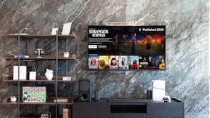 A modern living room with a marble wall, a mounted TV displaying 'Stranger Things', and shelves with board games. - Luxury 2BR Burj Khalifa View Dubai Mall (Dubai)
