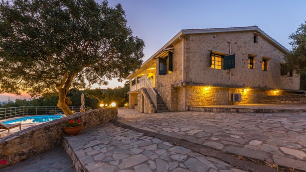 Un edificio de piedra con piscina, iluminación exterior y una escalera que lleva a la entrada.