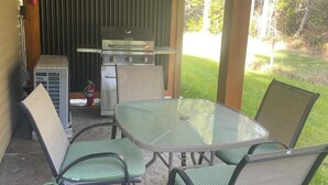 An outdoor patio with a glass table and chairs, a grill, and a fire extinguisher. - Quiet getaway in the forest close to beach/lakes/Mt Washington and great food. (Qualicum Beach)