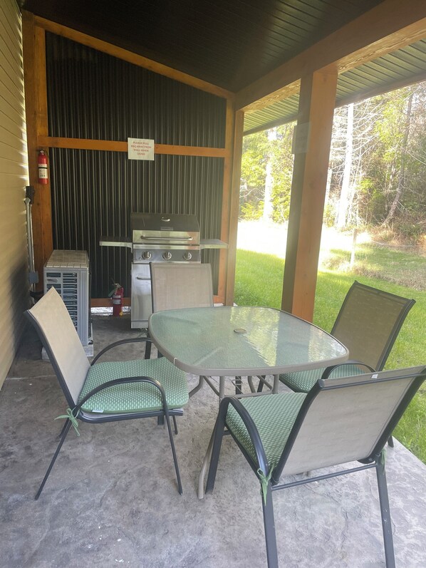 Un patio exterior con una mesa y sillas de vidrio, una parrilla y un extintor.