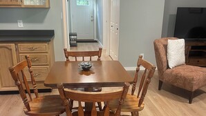 A dining area with a wooden table and chairs, a kitchen with wooden cabinets, and a TV in the background. - Quiet getaway in the forest close to beach/lakes/Mt Washington and great food. (Qualicum Beach)