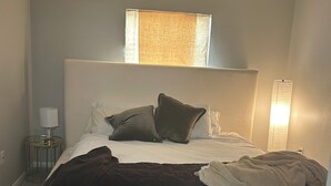 Ein Schlafzimmer mit einem Bett, einem Nachttisch, einer Lampe und einem Fenster.