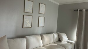 Ein Wohnzimmer mit einem beigefarbenen Sofa, einem Deckenventilator und vier gerahmten Kunstwerken an der Wand.