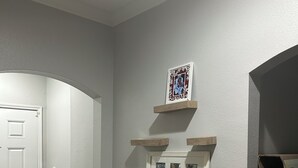 Ein Flur mit einer weißen Tür, Holzboden und einem an der Wand befestigten Regal mit gerahmten Fotos.