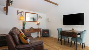 Una sala de estar con un sofá de cuero marrón, una mesa de centro de madera, una mesa de comedor con sillas, una chimenea, un televisor de pantalla plana y un espejo en la pared.