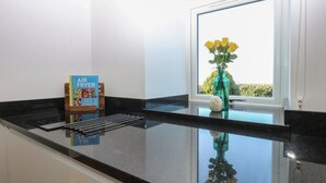 Una encimera de cocina con un libro titulado 'AIR FRYER', un jarrón verde con flores amarillas y una ventana que da a vistas de vegetación.