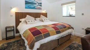 Un dormitorio con una cama, cabecera de madera, un cuadro sobre la cama, una ventana y una mesita de noche.