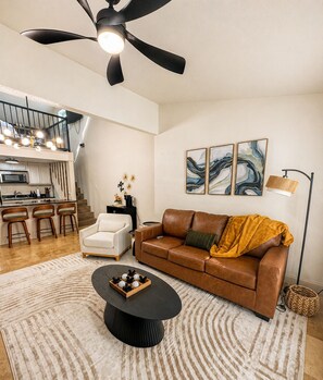 Ein modernes Wohnzimmer mit einer braunen Ledersofa, einem weißen Sessel, einem schwarzen Couchtisch und abstrakter Wandkunst.
