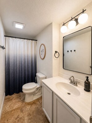 Ein Badezimmer mit Toilette, Waschbecken, Spiegel und Duschvorhang.