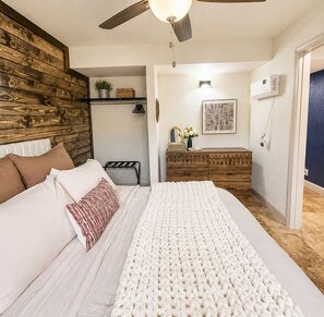 Ein Schlafzimmer mit Bett, Deckenventilator, Kommode und Wand-Klimaanlage.