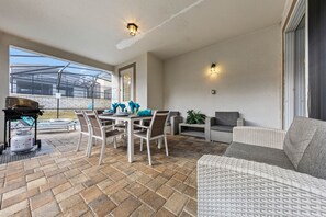 Eine Terrasse im Freien mit Tisch, Stühlen, einer Rattan-Couch und einem Grill.