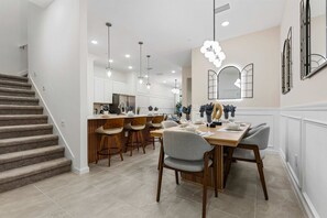 A modern kitchen with a dining area, wooden bar stools, and pendant lighting. - 5Br & 5Ba Paradiso Grande - Walk To Seaworld 10507 (Orlando)