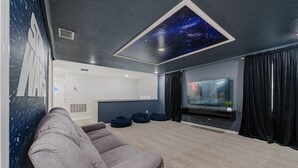A modern living room with a large flat-screen TV, a ceiling with a starry sky design, a grey sofa, and a dark carpet. - 6Bd Villa W Spa, Star Wars Cinema & Gameroom 2088 (Kissimmee)