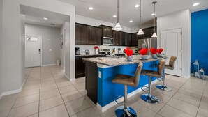 A modern kitchen with dark cabinets, a central island with bar stools, and a blue accent wall. - Modern 5Br Downstairs Room, Pool & Lazy River 2402 (Kissimmee)