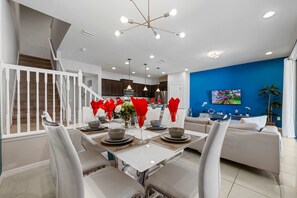 A modern dining area with a white table set for four, a staircase, and a blue accent wall. - Modern 5Br Downstairs Room, Pool & Lazy River 2402 (Kissimmee)