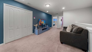 A hallway with a grey couch, a TV on a stand, and a door with a blue wall. - Modern 5Br Downstairs Room, Pool & Lazy River 2402 (Kissimmee)